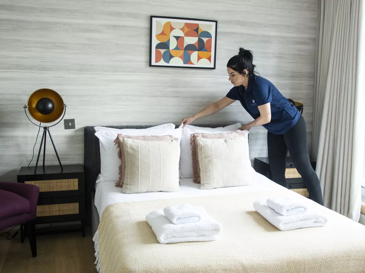 UF Cleaning housekeeper preparing a bright hotel bedroom
